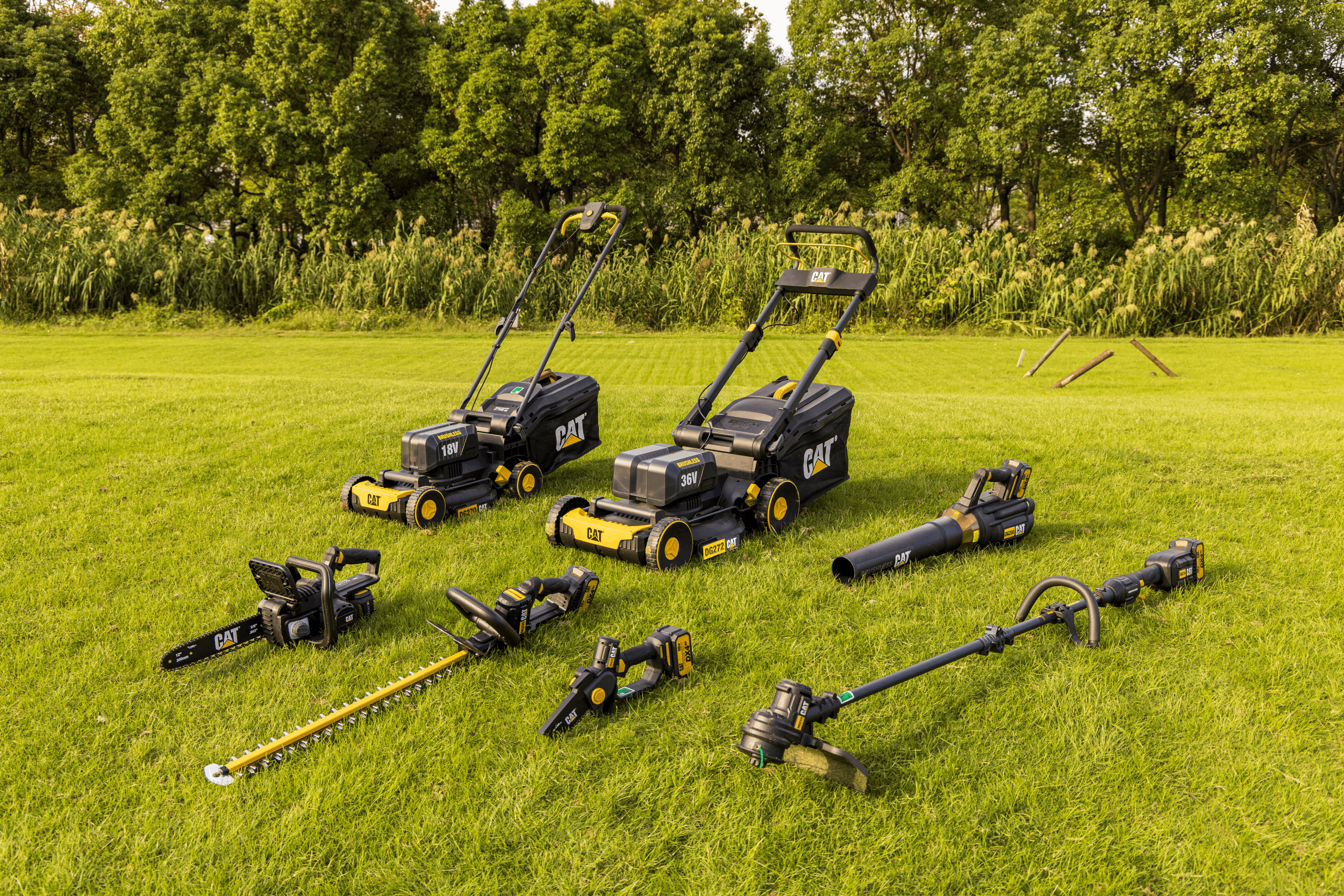 Set of lawn care tools including mowers, hedge trimmers, and strimmers on a grassy field with trees in the background.